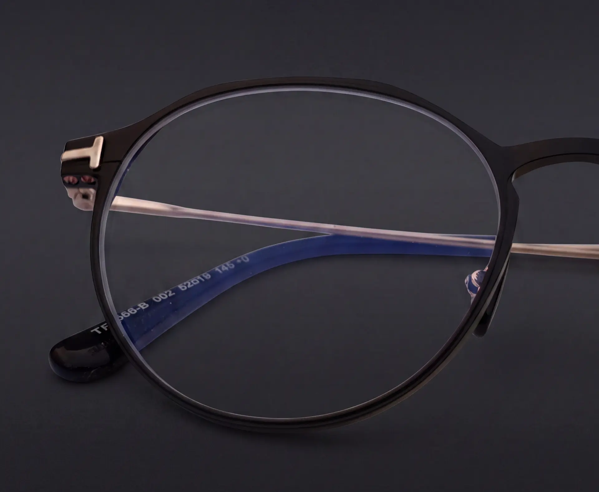 Prim-plan lentilă Tom Ford cu filtru blue-light și marcaj TF pe ramă neagră rotundă