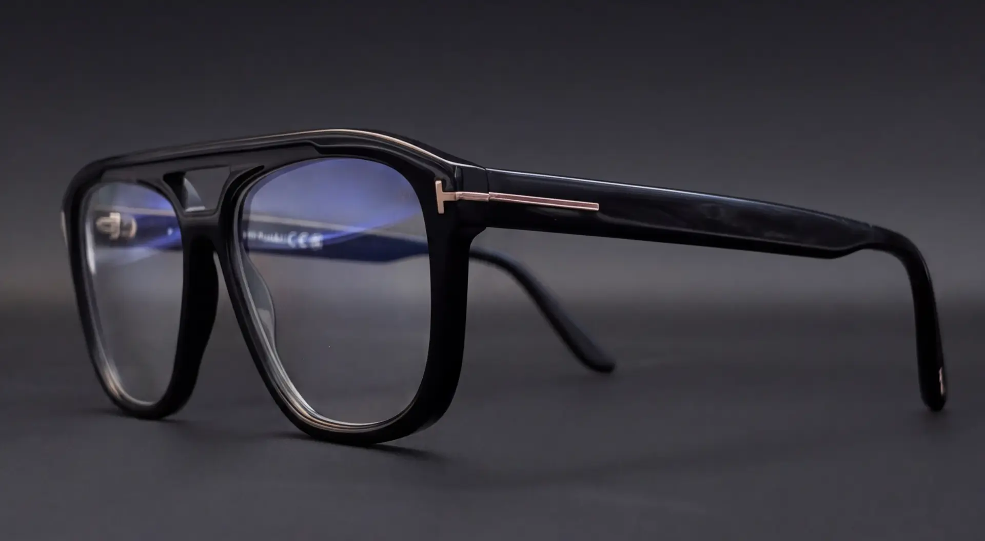 Ramă Tom Ford neagră tip aviator văzută din profil, cu braț gros și detaliu metalic auriu
