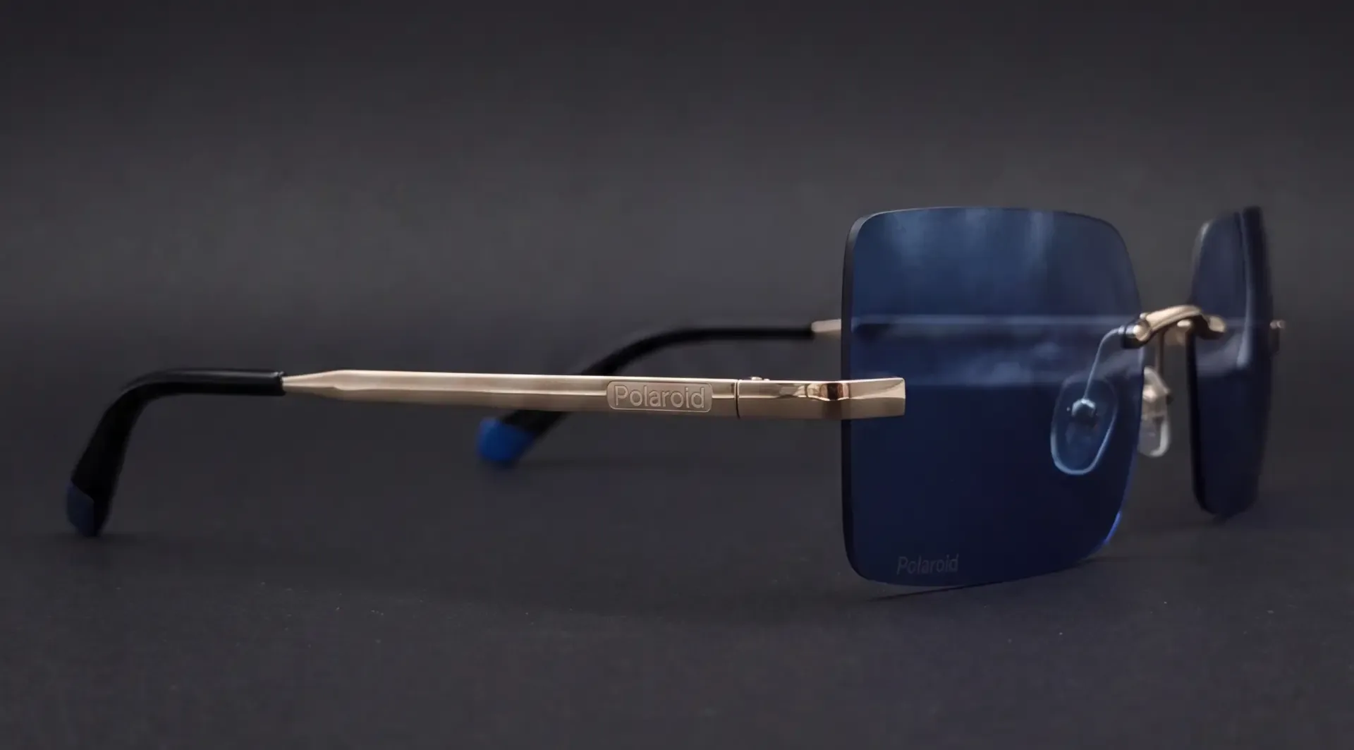 Ochelari de soare Polaroid rimless cu lentilă albastră, vedere din profil, braț auriu cu logo Polaroid