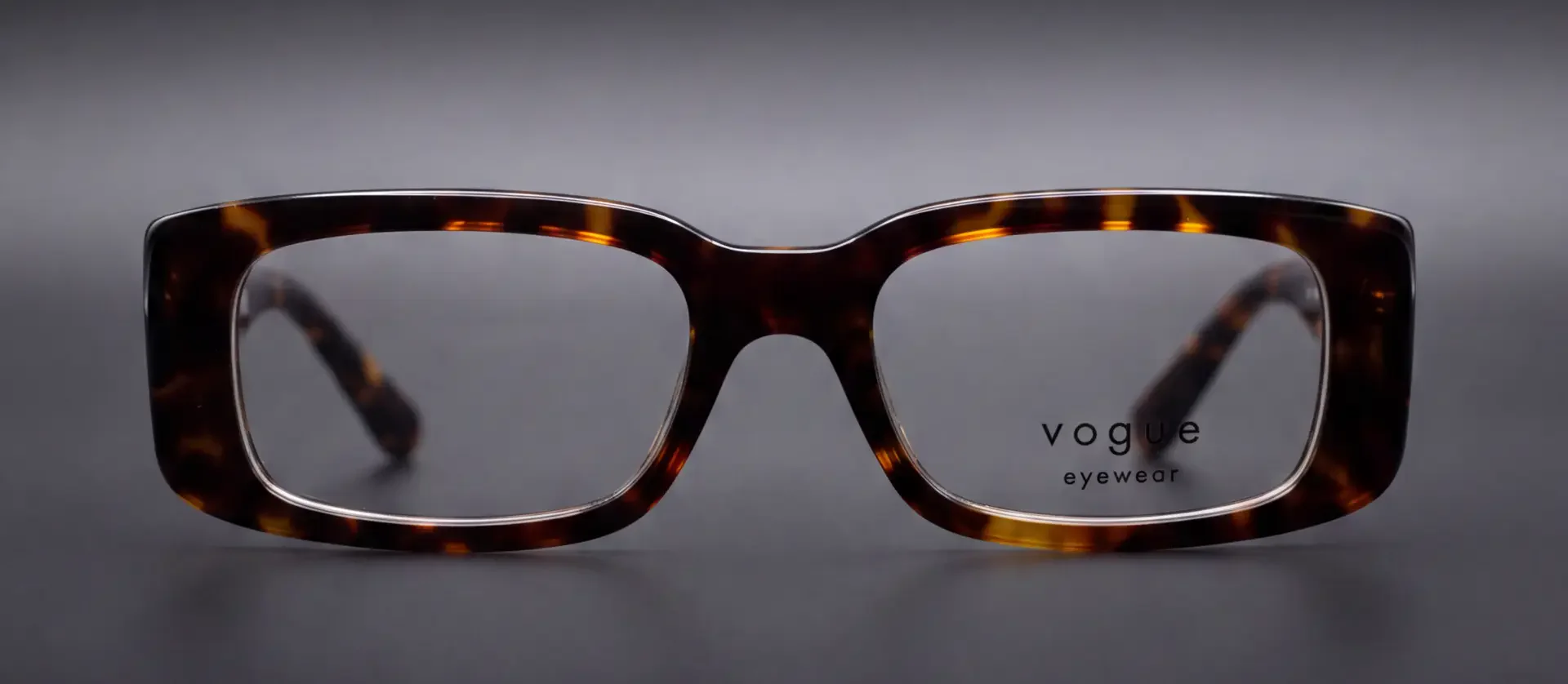 Ramă Vogue tortoise rectangulară, vedere frontală cu inscripția Vogue pe lentilă, disponibilă la ArenaMed Optics