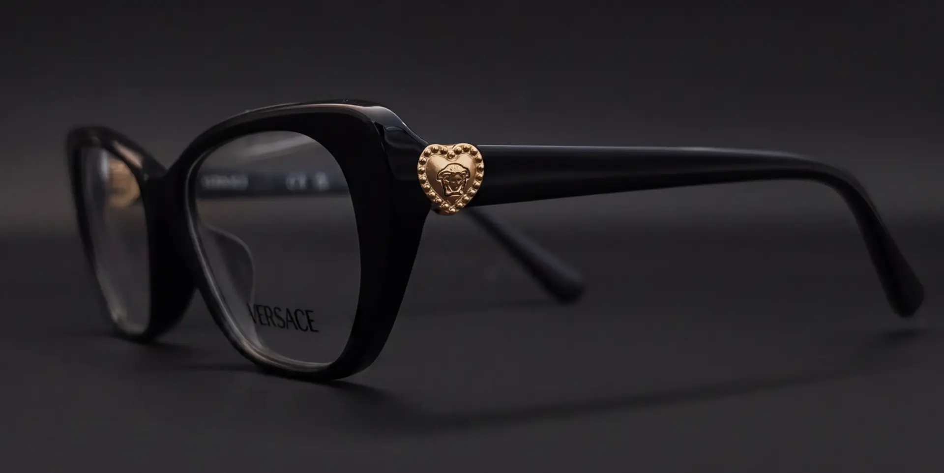 Ramă Versace neagră văzută din profil, cu medalion Medusa auriu în formă de inimă pe braț