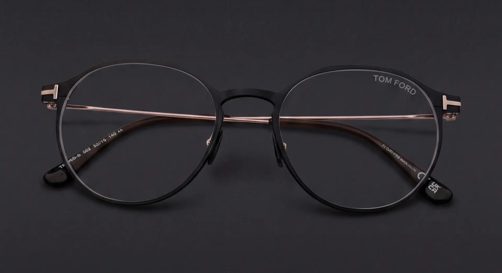 Ramă Tom Ford rotundă neagră cu punte și brațe aur roze, vedere frontală, disponibilă la ArenaMed Optics