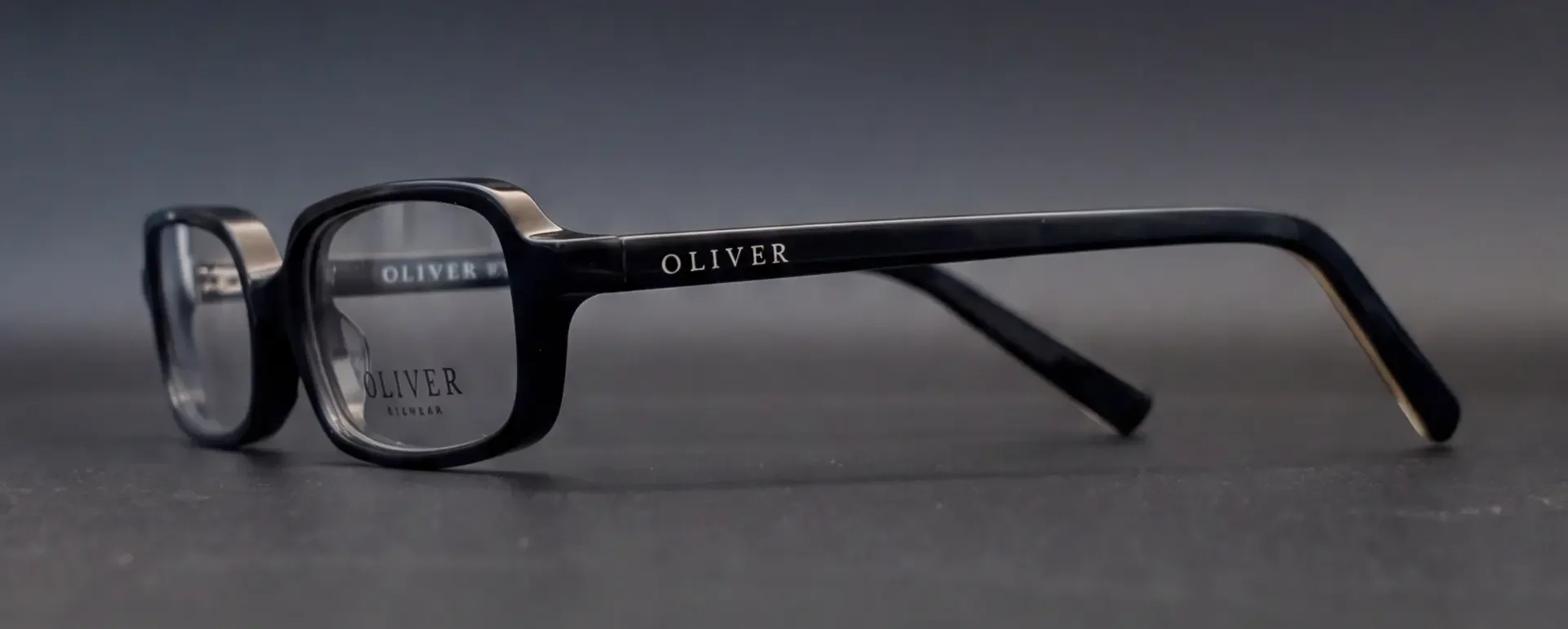 Ramă Oliver Eyewear neagră văzută din profil, cu logo pe braț, disponibilă la ArenaMed Optics