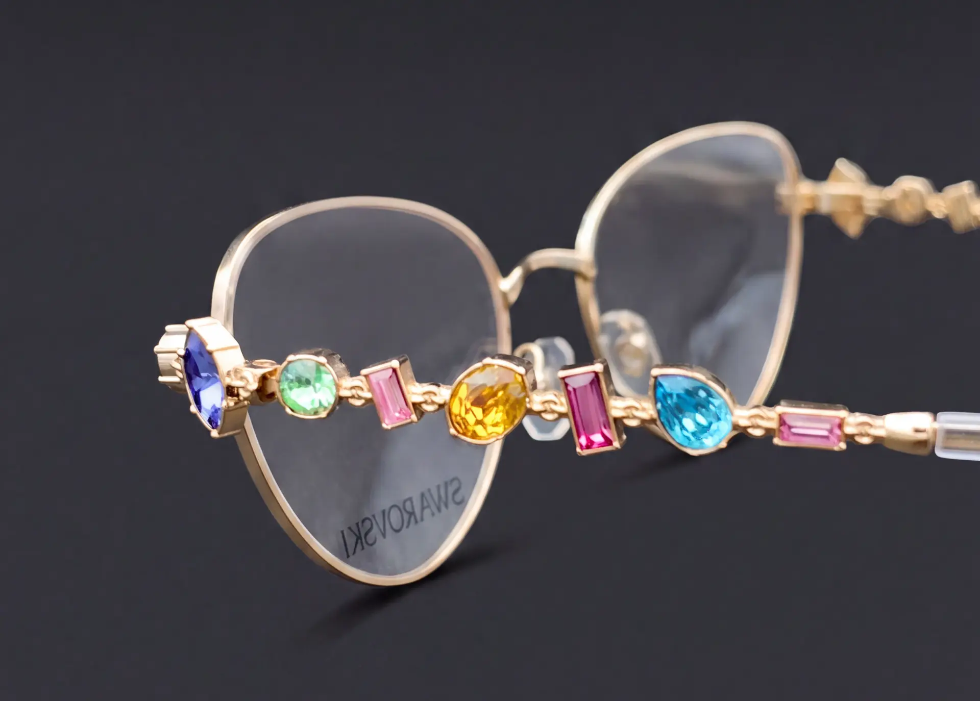 Detaliu braț ramă Swarovski aurie cu cristale albastre, verzi, galbene și roz